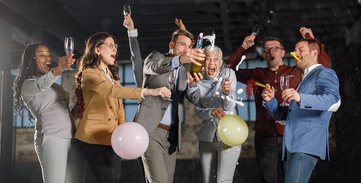 Cheerful entrepreneurs splashing while opening champagne at office party.